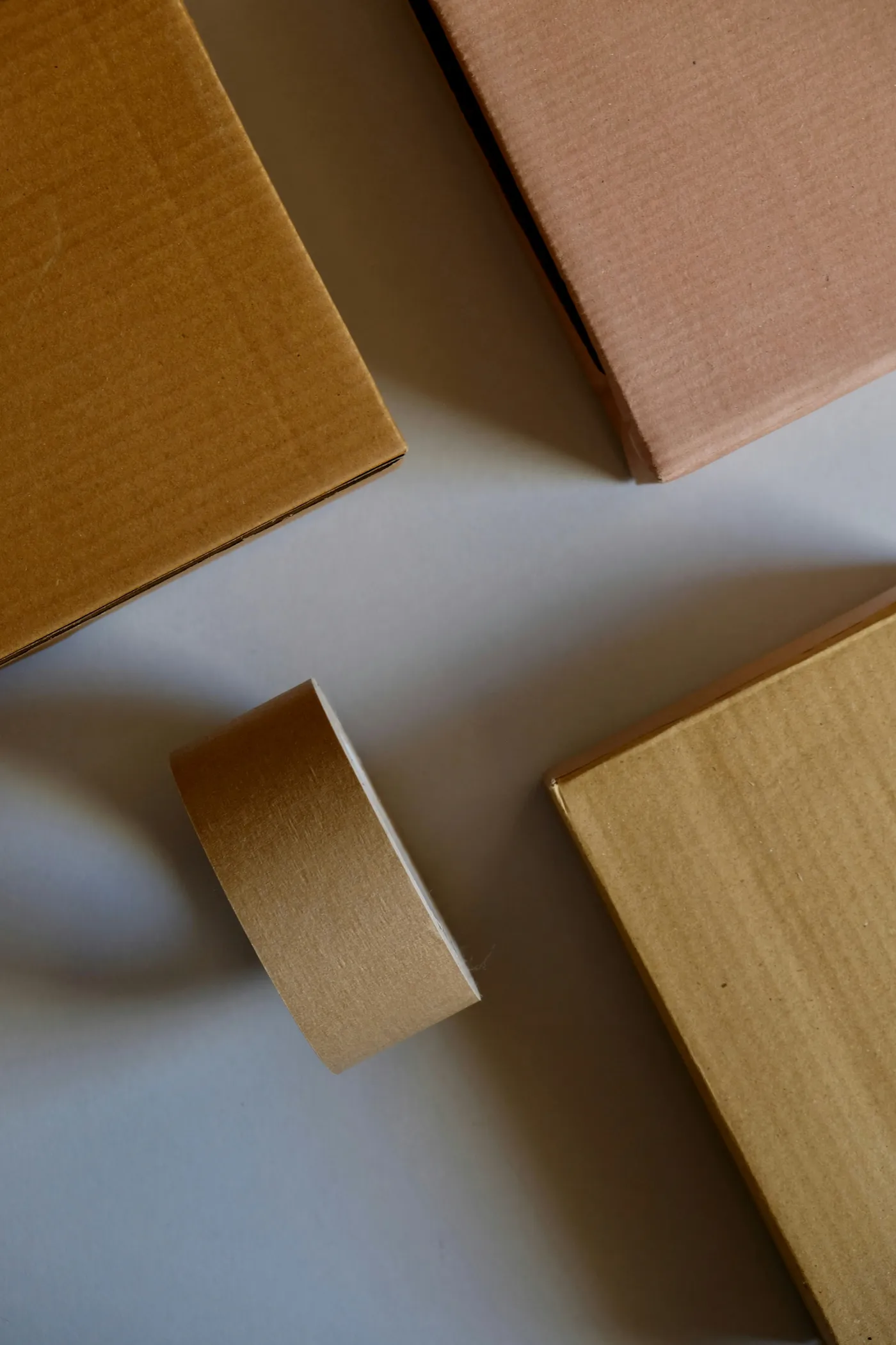 A roll of natural kraft paper tape beside sealed kraft cardboard bottle boxes
